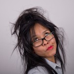 Crazy or frazzled looking Asian woman with bright lipstick and ruffled hair pulling a face while looking up.